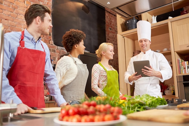Photo cours de cuisine, concept culinaire, alimentaire, technologique et humain - amis heureux avec tablette pc dans la cuisine
