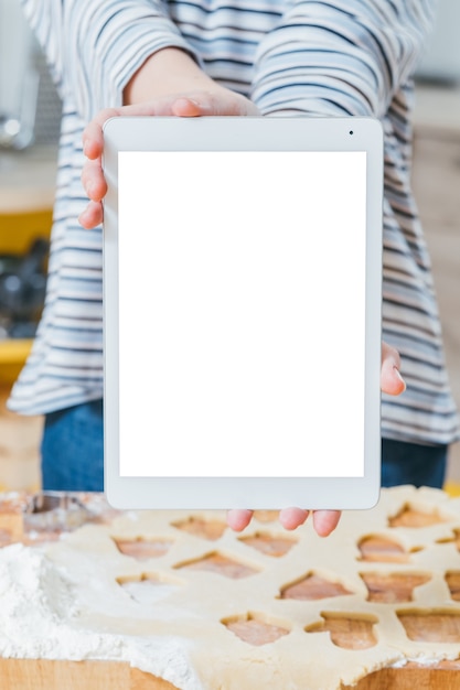 Cours culinaire en ligne. Gros plan de l'écran de la tablette blanche. Femme tenant le dispositif sur la pâte roulée sur la table.