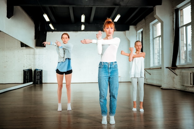 Cours de danse moderne. Professeur de danse moderne professionnel aux cheveux rouges à la recherche de sérieux tout en montrant des mouvements à ses élèves