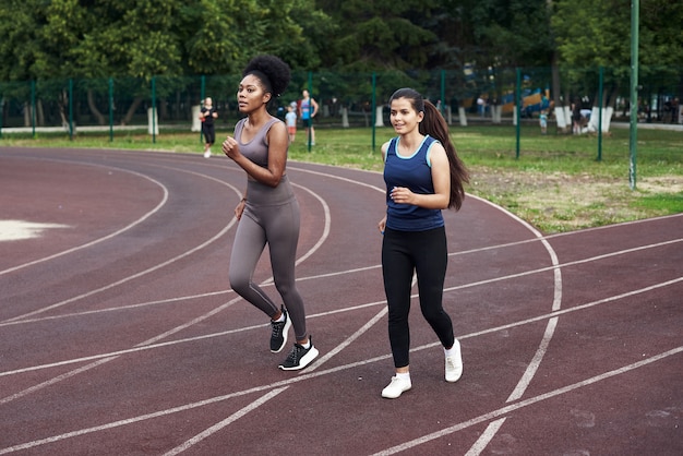 Cours de fitness dans la rue. De belles copines courent sur la piste de sport du stade.