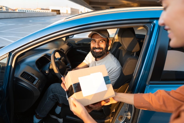 Photo un coursier arabe donnant une boîte à colis au client depuis sa voiture
