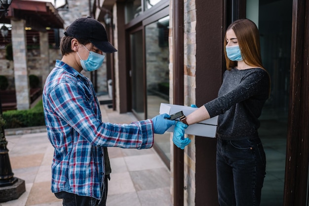 Un coursier portant un masque de protection et des gants médicaux livre des plats à emporter Service de livraison dans des conditions de pandémie de coronavirus covid19 d'épidémie de maladie de quarantaine