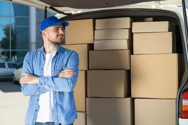 Un coursier avec une tablette dans les mains près d'une voiture avec des cartons