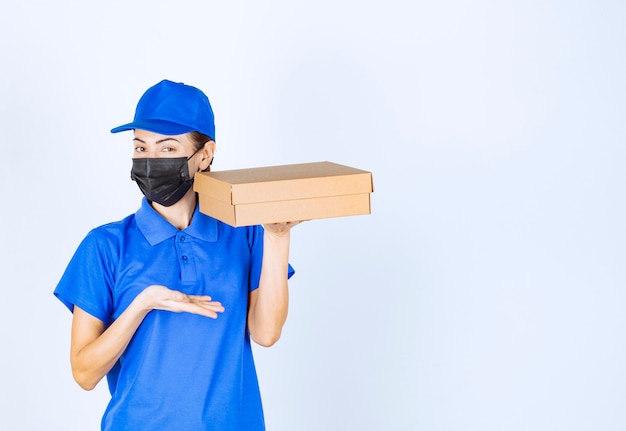 Coursière en uniforme bleu et masque facial livrant une boîte en carton au client.