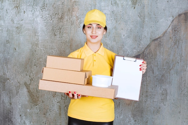 Coursière en uniforme jaune livrant plusieurs boîtes en carton et tasses à emporter et présentant le blanc pour signature