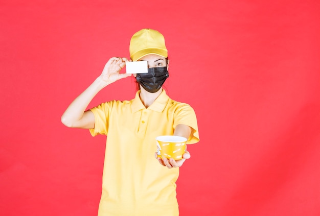 Une coursière en uniforme jaune et masque noir livre une tasse de nouilles et présente sa carte de visite