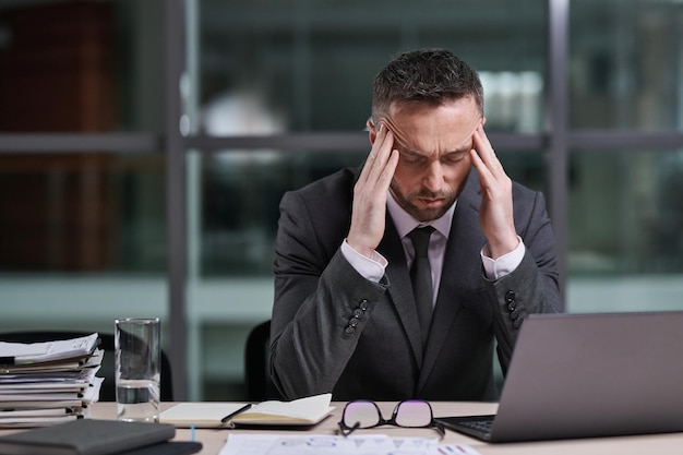 Courtier masculin fatigué et stressé touchant les temples tout en se penchant sur le lieu de travail