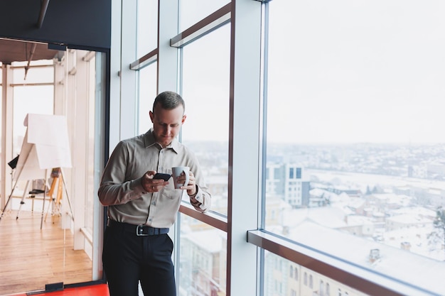 Courtiers masculins avec téléphone regardant vers la fenêtre avec café à la main dans un espace de travail moderne