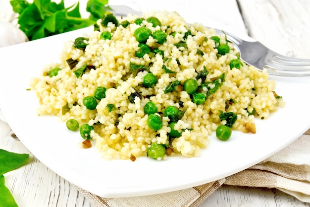 Couscous aux épinards et petits pois dans une assiette sur un torchon, basilic et fourchette sur fond de planche de bois