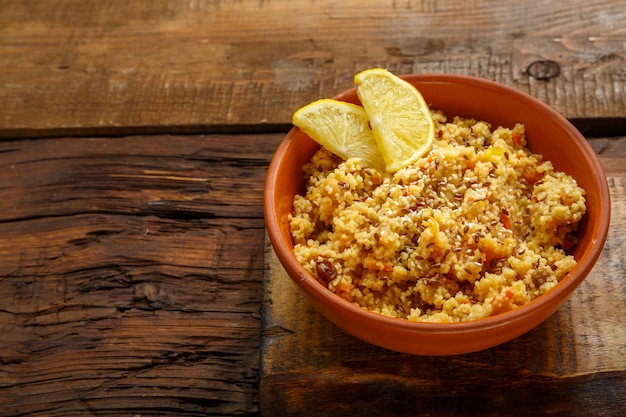 Couscous masfouf aux fruits secs et noix dans une assiette d'argile sur une planche de bois sur la table