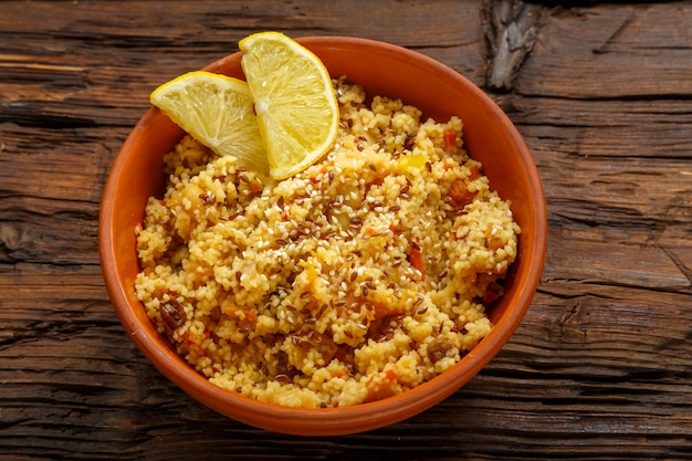 Couscous masfouf aux fruits secs et noix dans une assiette d'argile sur une table en bois Photo horizontale