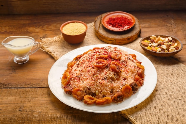 Couscous masfouf aux fruits secs et noix sur une table en bois à côté de gruau de safran et de couscous