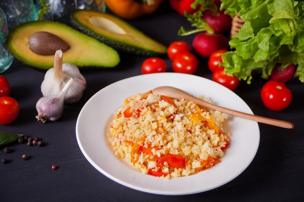 Couscous végétarien maison délicieux avec des tomates, des carottes, du poivre et du basilic frais sur une table de cuisine sombre avec des légumes sur le fond