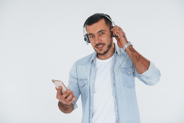 Écoute de la musique dans les écouteurs Jeune bel homme debout à l'intérieur sur fond blanc