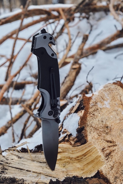 Le couteau de camping pliant est coincé dans une souche de pins tombés dans la forêt d'hiver