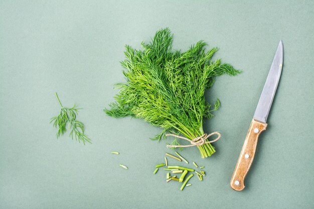 Photo un couteau coupe les tiges d'un tas d'aneth frais sur un fond vert de vitamines vertes