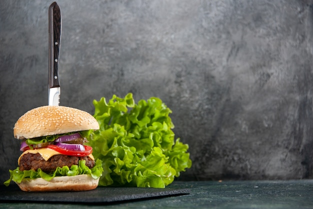 Couteau dans un délicieux sandwich et vert sur un plateau noir sur le côté droit sur une surface claire à moitié sombre avec un espace libre