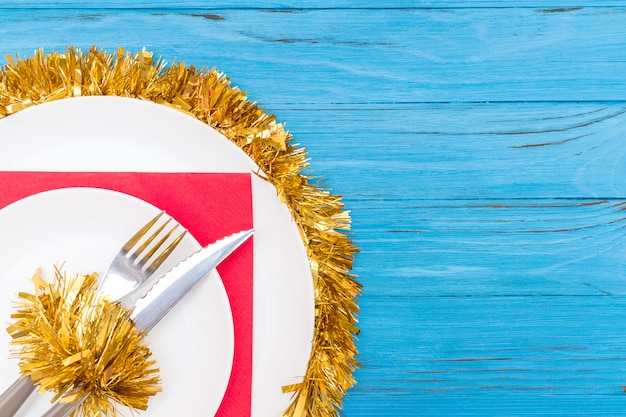 Un couteau et une fourchette en plaque blanche sur une serviette rouge décorée d'un clinquant de Noël