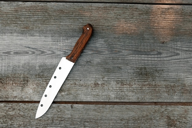 Un couteau à manche brun repose sur un gris en bois. fond
