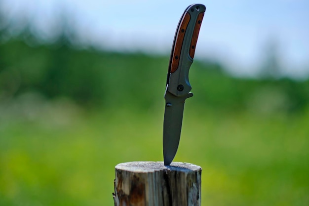 Un couteau pliable est coincé dans une souche de bois contre le fond de la forêt Outil pour les loisirs en plein air