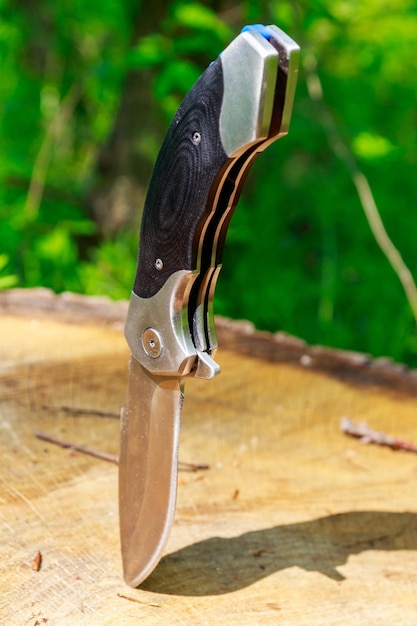 Couteau pliant qui sort d'une souche en bois dans la forêt verte