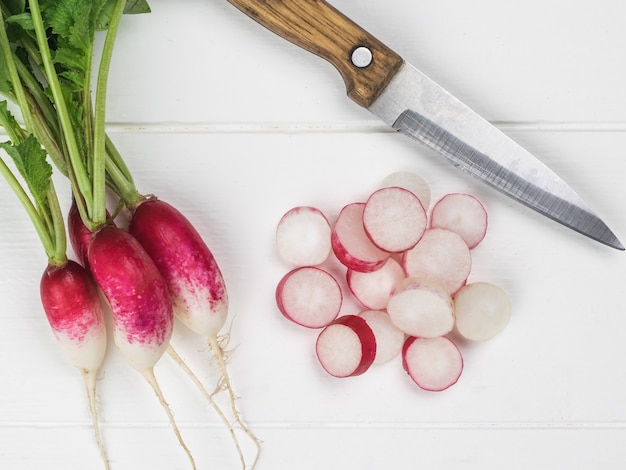Un couteau et des radis tranchés sur une table en bois blanc. Une nouvelle récolte de radis.