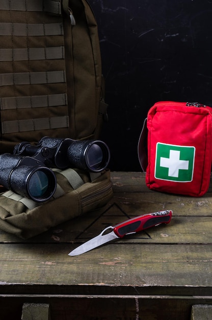 Photo couteau suisse et trousse de premiers soins jumelles et sac à dos militaire sur une boîte militaire cadre vertical trousse de premiers soins et couteau
