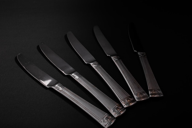 Des couteaux en métal argenté se trouvent sur un fond noir avec un éclat de lumière