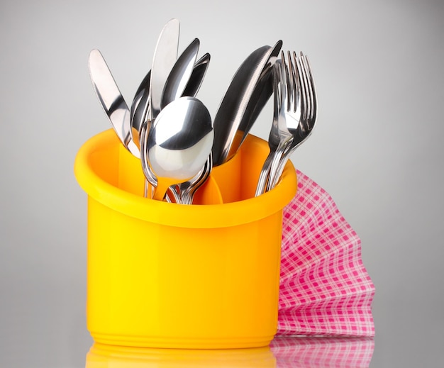 Coutellerie de cuisine couteaux fourchettes et cuillères en support jaune avec serviette rose sur fond gris