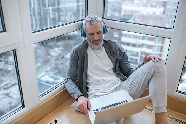 Écouter quelque chose. Un homme mûr avec un ordinateur portable et des écouteurs écoutant quelque chose sur internet