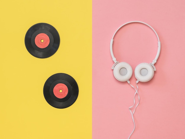 Écouteurs blancs et disques vinyles rouges sur fond jaune et rose. Technique rétro pour jouer de la musique.