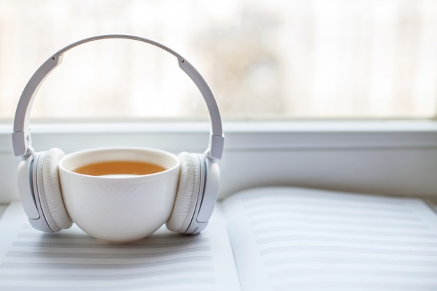 Écouteurs blancs avec une tasse de thé sur la fenêtre