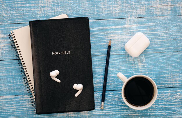 Écouteurs pour ordinateur portable Bible et tasse à café sur fond de bois bleu, espace de copie plat