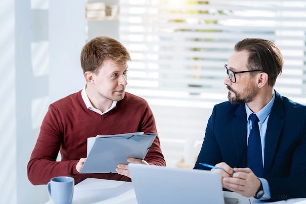 Écoutez-moi. Attrayant et agréable deux collègues masculins discutant des inconvénients tout en se regardant et assis à la table