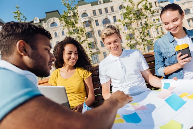 Écoutez-moi. Des étudiants ravis assis sur le banc et gardant le sourire sur les visages tout en regardant le papier Whatman