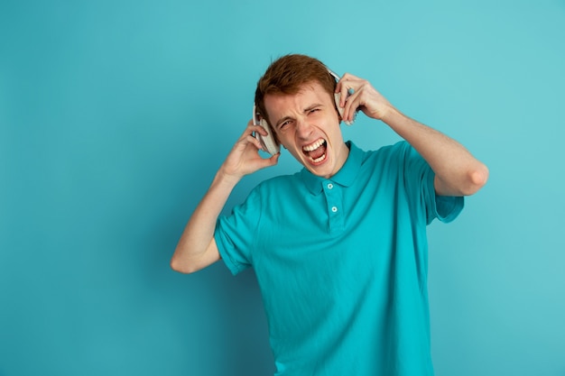 Écoutez de la musique, fou. Portrait moderne du jeune homme caucasien isolé sur mur bleu, monochrome. Beau modèle masculin. Concept d'émotions humaines, expression faciale, ventes, publicité, tendance.