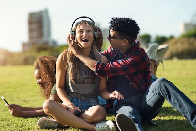 Écoutez Photo de deux jeunes amis joyeux écoutant de la musique sur des écouteurs à l'extérieur dans un parc pendant la journée