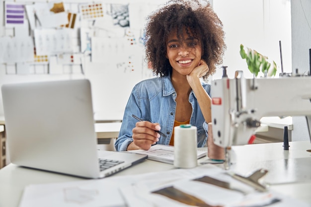 Une couturière afro-américaine dessine en regardant une leçon en ligne via un ordinateur portable dans un studio lumineux