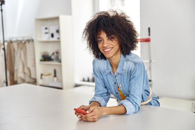 Une couturière afro-américaine tient un téléphone portable s'appuyant sur une grande table de coupe en atelier