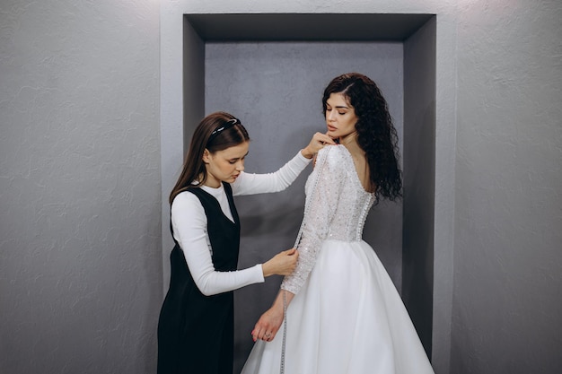 Couturière aidant la mariée à mettre sa robe de mariée dans un magasin de vêtements