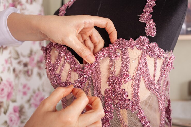 La couturière coud de la dentelle et des perles à la robe rose
