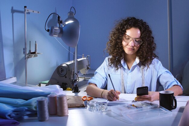 Couturière écrit des notes dans le journal à la table.