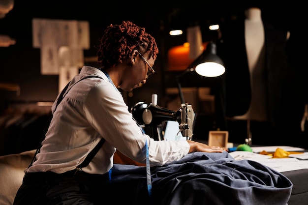 Couturière expérimentée cousant des vêtements textiles pour une commission vestimentaire sur mesure d'un prochain client. Couturier qualifié utilisant une machine à coudre professionnelle dans l'espace de travail de l'atelier