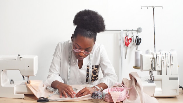 Couturière femme afro-américaine, créatrice de mode écoutant de la musique avec des écouteurs tout en travaillant sur le tissu dans l'atelier du Studio