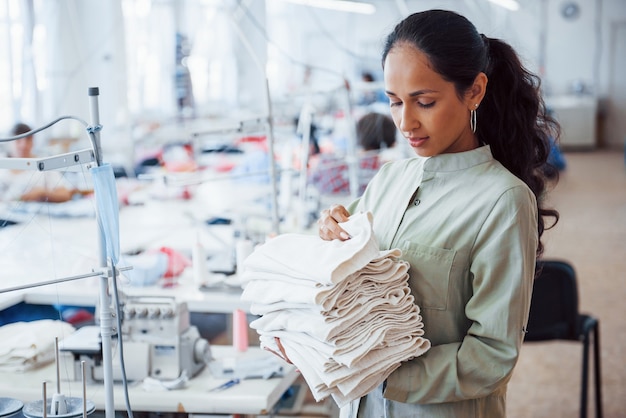 Une couturière se tient dans l'usine avec un chiffon dans les mains.