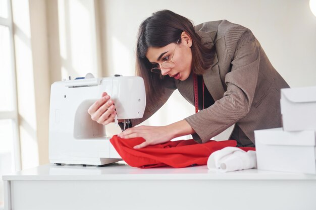 Couturière travaille avec un tissu rouge Jeune femme en vêtements formels est à l'intérieur Conception de style