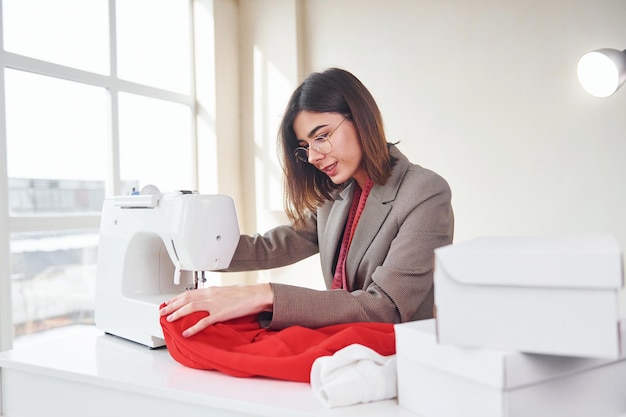 Couturière travaille avec un tissu rouge Jeune femme en vêtements formels est à l'intérieur Conception de style