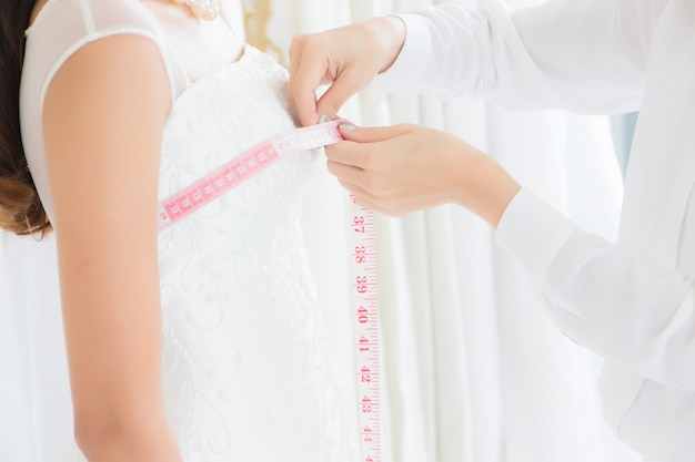 La couturière utilise un ruban à mesurer pour mesurer la taille du buste d'une cliente qui a commandé une robe de mariée dans un atelier de couture.