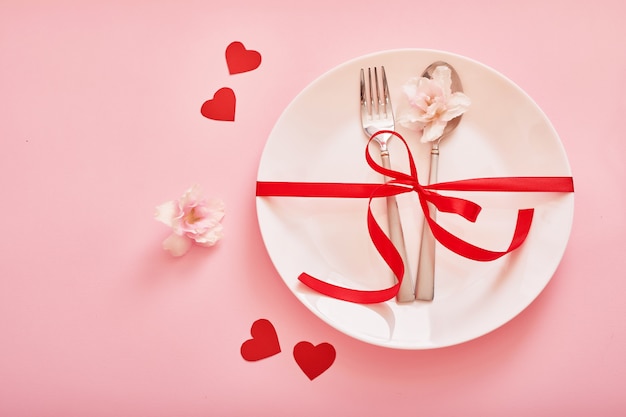 couverts et une assiette avec des coeurs sur une surface rose pour la Saint-Valentin