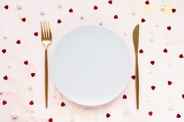 Couverts en or et assiette sur rose avec des coeurs. Concept de Saint Valentin, repas, dîner et date